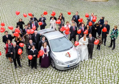Hochzeitsgesellschaft mit roten Ballons um Auto bei Hochzeit nahe Dillingen, festgehalten vom Hochzeitsfotografen.
