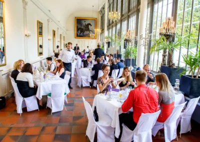 Gäste sitzen bei der Hochzeitsfeier an runden Tischen im Palmenhaus Schloss Nymphenburg in München.