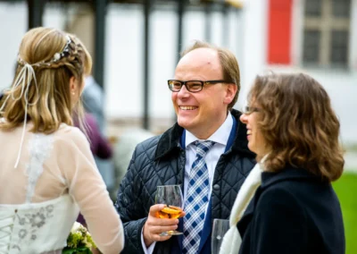 Hochzeitsfoto bei Schloss Gruenau: Drei Gaeste im Gespraech mit Getraenken auf der Hochzeit. Hochzeitsfotografie.