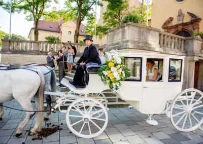Braut in Kutsche mit Blumenarrangement, Hochzeitsfotografie in Schwabing Muenchen, stilvolle Atmosphaere.