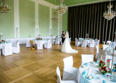 Hochzeit in Ansbach: Brautpaar tanzt in elegantem Saal mit gedeckten Tischen und Kronleuchtern. Hochzeitsfotografie.