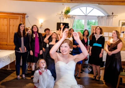 Brautstrausswurf bei einer Hochzeit, lachende Frauen im Hintergrund, Aschbacher Hof, Hochzeitsfotografie.