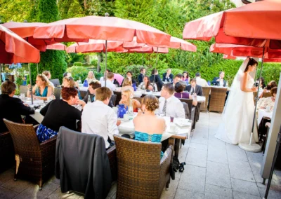 Hochzeitsfeier im Freien mit Gaesten unter roten Sonnenschirmen im Hotel Seehof.