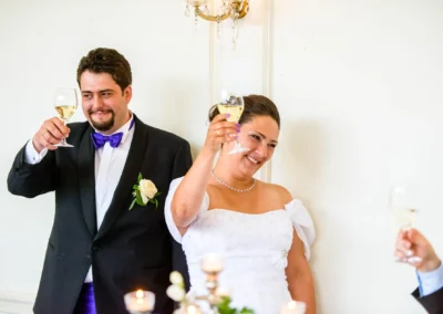 Brautpaar hebt Gläser bei Hochzeit im Palmenhaus Schloss Nymphenburg in München, festgehalten von Hochzeitsfotograf.
