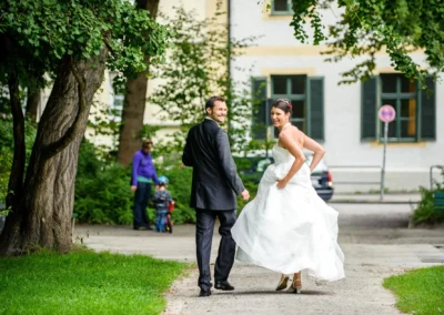Brautpaar lacht beim Spaziergang im Pasinger Stadtpark. Hochzeitsfoto in Muenchen zeigt Freude und Eleganz.