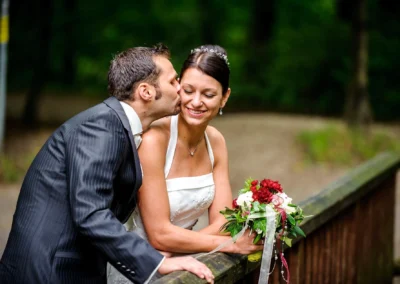 Brautpaar auf Bruecke im Pasinger Stadtpark, der Bräutigam küsst die Braut. Hochzeitsfotografie aus München.