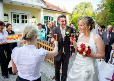 Brautpaar stoesst mit Gaesten in Schwabing auf Hochzeit an, Braut mit Blumenstrauss. Hochzeitsfotografie Muenchen.