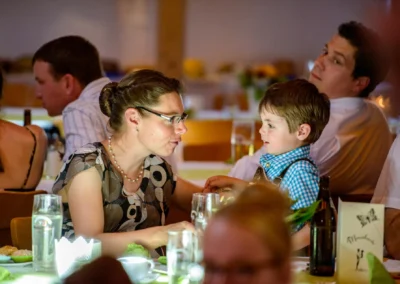 Mutter im Gespraech mit Jungen bei Hochzeitsfeier nahe Rosenheim, festlich gekleidete Gaeste im Hintergrund.