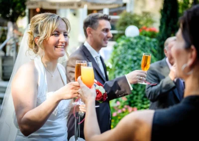 Brautpaar stoßt mit Sekt an. Aufnahmen einer Hochzeit in Schwabing. Entspannte Hochzeitsreportage in einer Gruenanlage.