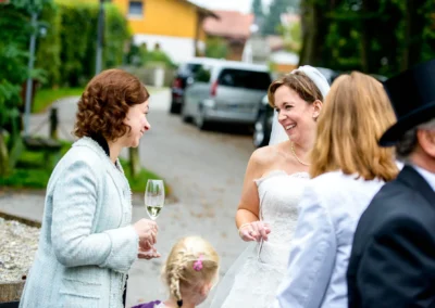 Lachende Braut in Aying im Gespraech mit Gaesten bei ihrer Hochzeit, aufgenommen von einem Hochzeitsfotografen.