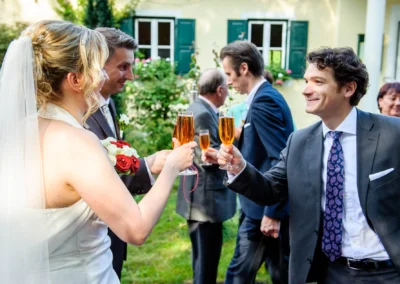 Brautpaar bei Hochzeitsfeier in Schwabing, Muenchen hebt Glaeser zum Anstossen im Freien