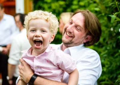 Lachender Junge in den Armen eines Mannes bei einer Hochzeit in Roehrmoos, festgehalten von einem Hochzeitsfotografen.