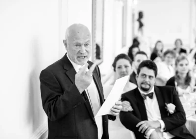 Älterer Herr hält Rede bei einer Hochzeit in München Nymphenburg, Gäste sitzen im Hintergrund, Hochzeitsfotograf.