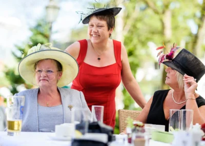 Drei Frauen in eleganter Kleidung bei Hochzeit in Bad Toelz, laecheln und unterhalten sich im Freien.