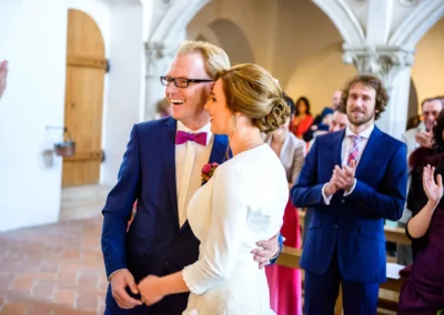 Brautpaar laechelt nach kirchlicher Trauung in Landshut. Gaeste klatschen im Hintergrund. Hochzeitsfoto von emotionalem Moment.