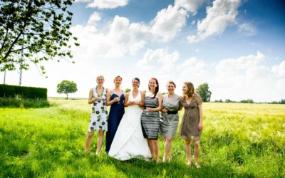 Sechs Frauen stehen fröhlich auf einer Wiese, die Braut in weißem Kleid, die anderen in Sommerkleidern, alle mit Drinks.
