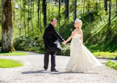 Brautpaar Hand in Hand auf Kiesweg im sonnigen Kurpark Bad Toelz, Hochzeitsfotografie in Oberbayern.