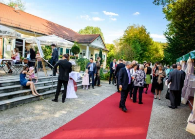 Hochzeitsgesellschaft auf rotem Teppich vor Festsaal in Schwabing, München. Hochzeit in entspanntem Freiluftambiente.