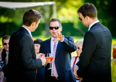 Hochzeitsreportage nahe Muenchen: Drei Maenner in Anzug im Gespraech bei einer Hochzeit im Freien.