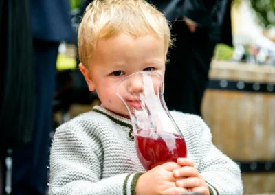 Kleiner Junge bei Hochzeitsfeier in Aying mit rotem Getränk in der Hand. Hochzeitsfoto von kirchlicher Trauung.