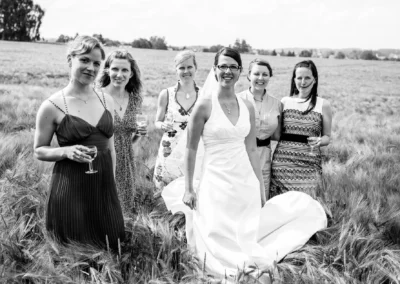 Braut und Gäste in einem Feld bei einer Hochzeit nördlich von München, alle lächelnd und mit Getränken.