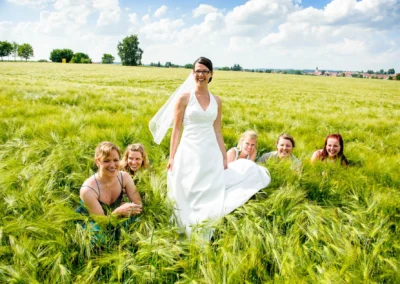Braut in weissem Kleid mit Freundinnen im Feld, aufgenommen bei Hochzeit nordlich von Dachau. Hochzeitsfotografie.