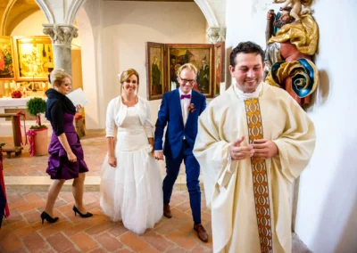 Brautpaar mit Priester bei kirchlicher Trauung in einer Kirche in Landshut, festliche Atmosphäre.