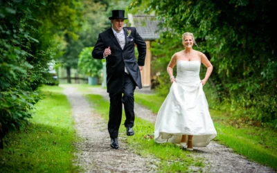 Brautpaar lacht und rennt auf einem Weg bei einer Hochzeit in Miesbach, umgeben von gruenem Laub.