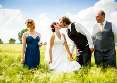 Brautpaar beim Kuss in einem Feld, begleitet von zwei Gästen, Hochzeitsfoto nördlich von München.