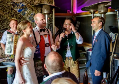 Brautpaar lacht mit Gästen bei einer Hochzeitsfeier in traditioneller Tracht. Hochzeitsfoto nahe Rosenheim.