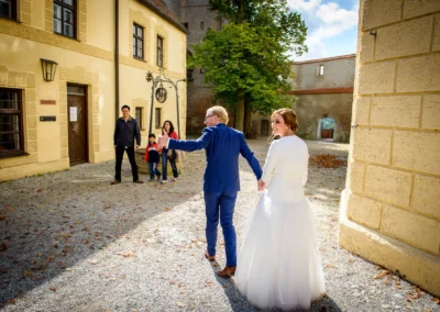 Brautpaar spaziert Hand in Hand im Hof, begleitet von Familie. Hochzeitsreportage bei Burg Trausnitz.