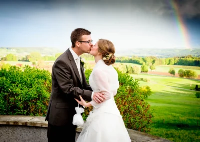 Brautpaar beim Kuss mit Regenbogen im Hintergrund, aufgenommen bei einer Hochzeit im Aschbacher Hof.