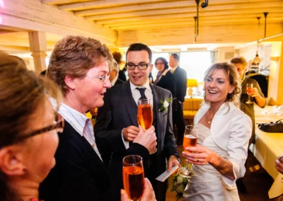 Hochzeitsfoto am Starnberger See: Lachende Gaeste stoßen mit Sekt glaesern an, aufgenommen von Hochzeitsfotograf.