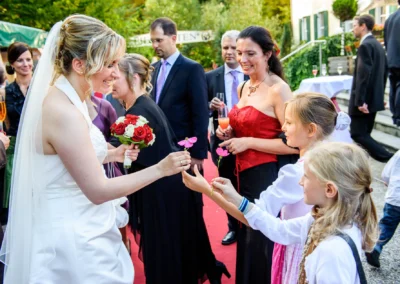 Braut verteilt Blumen an Kinder auf rotem Teppich bei Hochzeit in Schwabing, München. Hochzeitsfotograf vor Ort.