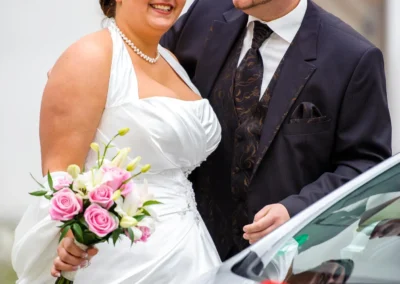 Brautpaar lacht bei ihrer Hochzeitsfotografie vor einem Auto, nahe Schloss Höchstädt an der Donau.