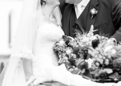 Brautpaar laechelnd vor Oldtimer, Hochzeitsportrait im Landkreis Muenchen, Hochzeitsfoto mit Blumenstrauss.