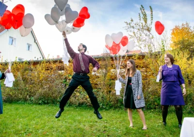 Mann springt mit roten und weissen Luftballons bei Hochzeit im Garten, Hochzeitsfoto bei alter Wirt Grunwald nahe Munchen.