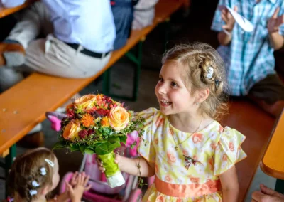 Kleines Mädchen mit Blumenstrauß bei Hochzeit nahe Rosenheim lächelt freudig, festgehalten von Hochzeitsfotograf.
