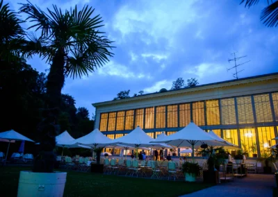 Abendstimmung bei einer Hochzeitsfeier im Palmenhaus Schloss Nymphenburg, beleuchtete Fenster und Sonnenschirme.