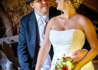 Braut und Bräutigam halten Hände in der Eventscheune Wallenburg, Hochzeit mit weißen und roten Blumenstrauß.