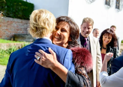 Lachende Frau umarmt Gast bei Hochzeit in Landshut, weitere Gaeste im Hintergrund, aufgenommen bei Hochzeitsreportage.