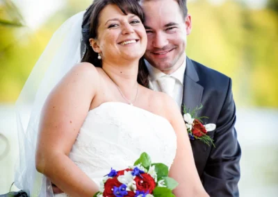 Glueckliches Brautpaar posiert mit Blumenstrauss bei Hochzeitsfotos nahe dem Wesslinger See.