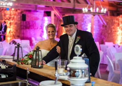 Brautpaar an der Bar der Eventscheune Wallenburg, laechelt in die Kamera. Hochzeitsreportage bei stilvoller Hochzeit.