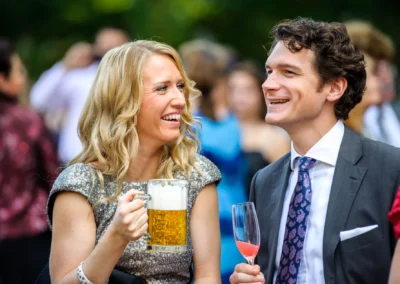 Frau und Mann lachen mit Bierkrug und Sektglas bei Hochzeit in Schwabing, Muenchen. Hochzeitsfotografie.