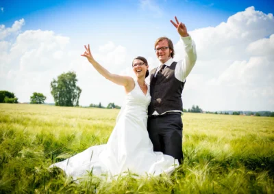 Brautpaar in einem Feld vor blauem Himmel, Hochzeit nördlich von Dachau. Hochzeitsfotograf zeigt freudigen Moment.