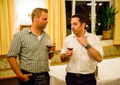 Zwei Männer mit Weingläsern unterhalten sich bei einer Hochzeit in Röhrmoos. Hochzeitsfotograf auf Landgasthof.