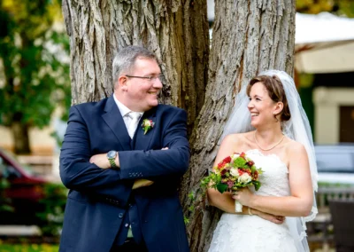 Brautpaar lacht an Baum gelehnt, Hochzeitsportrait in Aying, aufgenommen von Hochzeitsfotograf in Oberbayern.