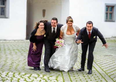 Brautpaar mit Begleitern lachend, Hochzeitsfotografie nahe Augsburg auf Kopfsteinpflaster vor Schlossportal.