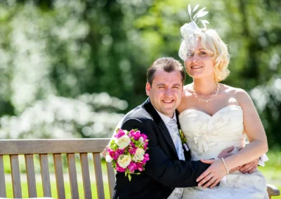 Brautpaar lacht auf einer Bank im Kurpark Bad Toelz, schoene Hochzeitsfotos in Oberbayern.