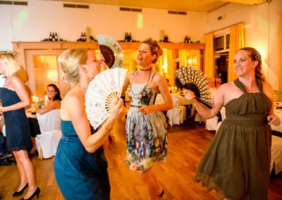 Tanzende Frauen mit Fächer bei Hochzeitsfeier in Röhrmoos. Hochzeitsfotografie fängt fröhlichen Moment ein.